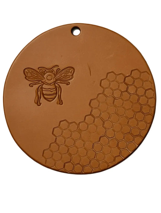 Brown round trivet with bee and honeycomb design on a white background